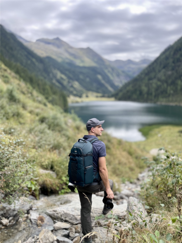 Jakob Günther mit Kamera und Rucksack, mit Blick auf den Riesachsee zwischen den Bergen