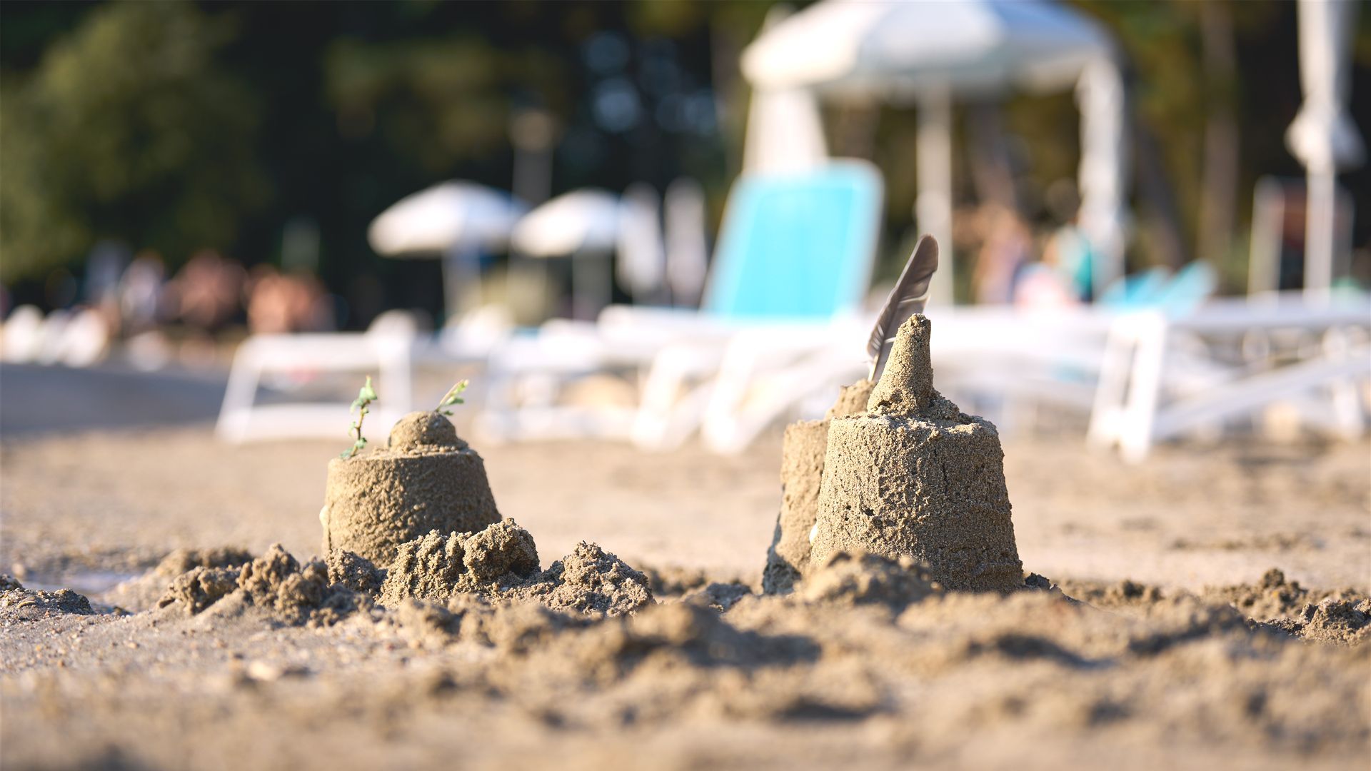 Sandburg am Strand, im Hintergrund Liegen und Sonnenschirme