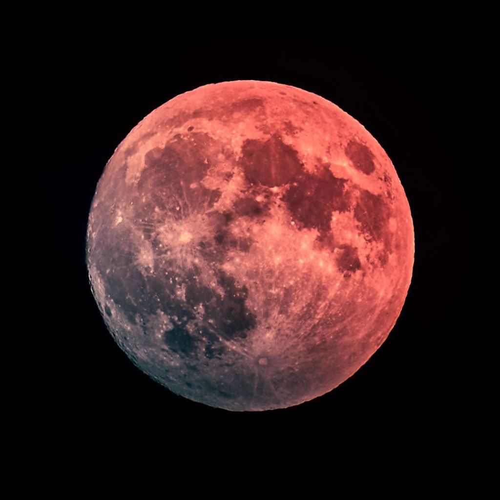 Vollmond im Oktober, rötlich beleuchtet, vor dunklem Hintergund.