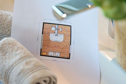 Ein Badplan auf Papier unter einer Armatur, daneben ein eingerolltes Handtuch