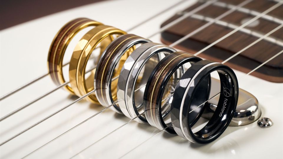 Sechs Ringe mit einer Einlage aus einer Gitarrensaite stehen zwischen den Saiten einer Gitarre