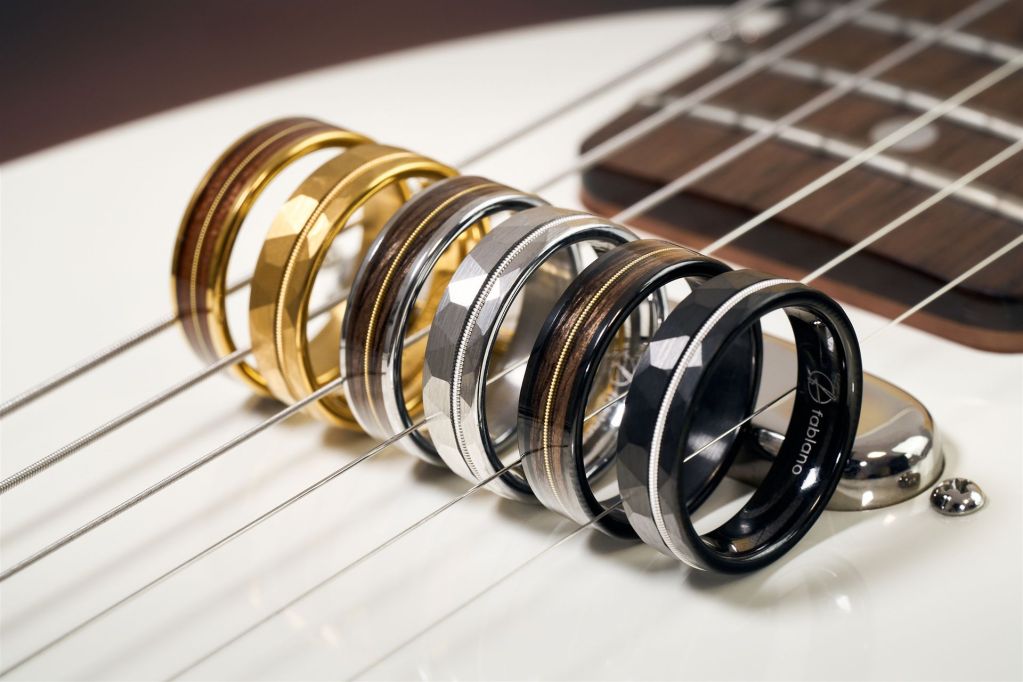Sechs Ringe mit einer Einlage aus einer Gitarrensaite stehen zwischen den Saiten einer Gitarre
