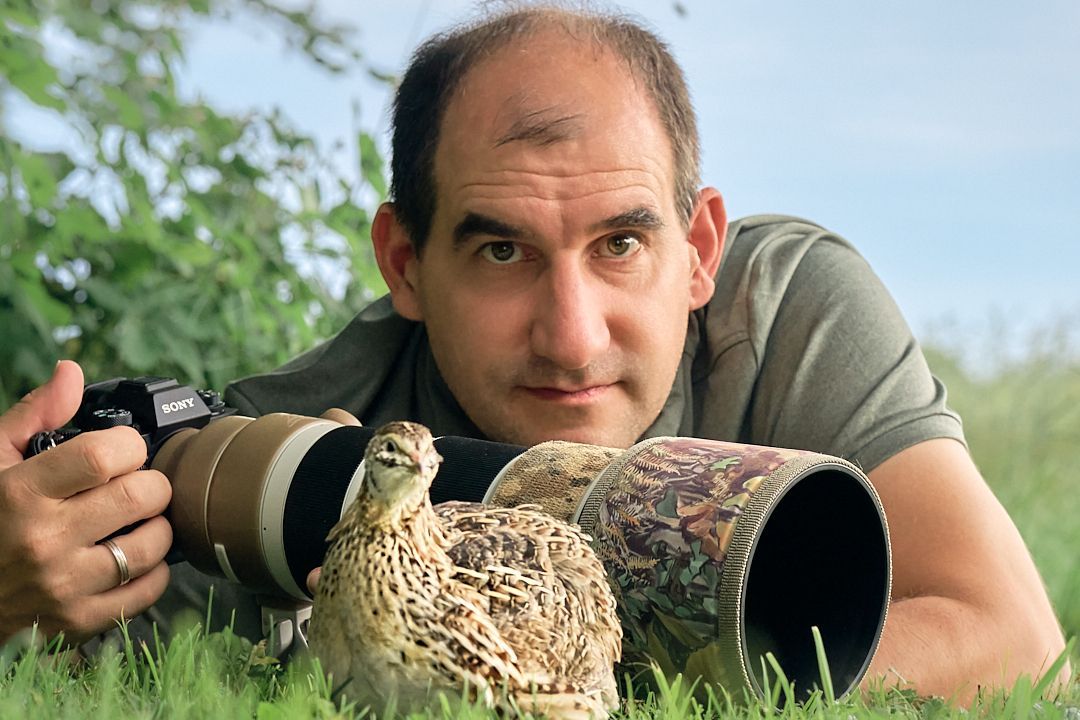 Portrait von Jakob Günther mit Kamera. Davor sitzt eine Wachtel im Gras.
